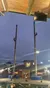 This image shows two people climbing tall poles during an outdoor event, with an audience and American flags below, set against an evening sky.