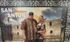 Two people are posing with smiles in front of a photographic backdrop that features the Alamo in San Antonio.