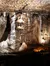 The image captures an impressive cave room adorned with an array of stalactites and stalagmites, illuminated to showcase their intricate details and textures, while a group of visitors at the bottom suggests the scale of the formations.