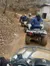 A group of people are riding all-terrain vehicles in a single file along a dirt trail in the woods.