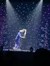 A performer is on stage under blue lights, seemingly engaged in an energetic act next to candy cane poles and a