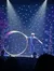 A performer on stage is holding a large hoop with a dazzling backdrop of blue lights as part of an entertainment event.