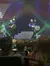 Two performers energetically playing drums on stage before an audience under colorful stage lighting.