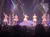 Five performers in golden dresses are dancing on stage in a festive setting with Christmas decorations.