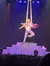 A performer is executing an aerial silk act with a partner in a dynamic pose against a starry backdrop on stage.