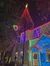 The image shows a night scene of a building and a tree festively adorned with vibrant Christmas lights, creating a cheerful holiday atmosphere.
