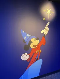 The image features the animated character Mickey Mouse in a magician's outfit pointing towards the sky with stars shining beside him.