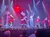 Performers in festive costumes, including Santa Claus, are on stage in a holiday-themed show with colorful stage lighting and a captivated audience.
