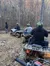 A group of people is taking a break while riding all-terrain vehicles through a leaf-covered forest trail.