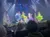 A group of performers in colorful dresses dance energetically on a festively decorated stage in front of an audience.