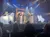 The image depicts a theatrical nativity scene with performers in costume on stage, surrounded by festive lights and decorations.