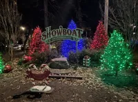 The image shows a festive Christmas display with trees lit in red, green, and blue lights, and a sign that reads 