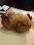 The image shows a roasted whole chicken placed on a plate, with a background of papers and a dimly lit setting.