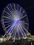 The image shows a brightly lit Ferris wheel at night, surrounded by colorful amusement park lights.