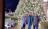 Three people are standing in front of a large, decorated Christmas tree at night.