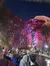 A group of people admire colorful lights decorating the trees along a riverside at night.