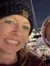 Two people wearing knit hats are smiling in a nighttime setting with city lights in the background.