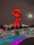 The image features a large, illuminated red sculpture against a night sky with people standing on a stone bridge, decorated with a Christmas wreath and lit up in colorful lights.