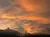 A vibrant sunset paints the sky with orange and yellow hues above silhouetted trees and clouds.