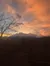 A picturesque sunset sky with orange and pink clouds is visible over a silhouetted landscape of trees and mountains.