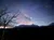 A serene twilight scene with silhouetted trees, a moonlit sky, and a line of clouds on the horizon.