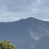 The image shows a mountain range under a cloudy sky with a few green trees in the foreground.