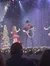 A cowboy-themed performer is seen on stage with a lasso, surrounded by dancers in a festive setting.