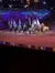 A group of riders on horses dressed in festive attire perform under twinkling lights and a wintry backdrop in an indoor arena.