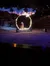 A horse with a rider is seen jumping through a flaming hoop in an arena with a backdrop of a fiery and starry night scene.