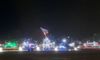 The image shows a nighttime scene with illuminated holiday lights, featuring various shapes and figures, including a depiction of the iconic Iwo Jima flag-raising, set against a dark sky.