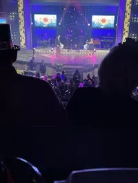 The image shows a live stage performance with two singers, a band, and an audience, featuring large digital screens displaying a sunflower.