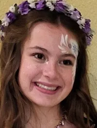 A woman dressed as a fairy stands smiling with five children in colorful outfits and face paint.