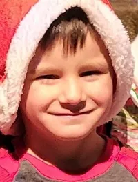 A group of children in holiday pajamas sit with an older woman dressed festively, posing for a Christmas-themed photo.