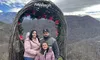 A family wearing winter clothing poses in front of a festive arch with mountains in the background.