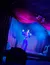 A performer in a sparkly outfit is singing on a stage illuminated by blue and purple lighting, with a draped backdrop.
