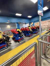People are seated in a Superman-themed roller coaster ride, preparing for takeoff.