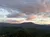 A scenic view of a lush, green mountainous landscape under a sky filled with soft, pink-tinged clouds.