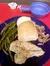 The image shows a plate with green beans, a grilled chicken breast, a dinner roll, mashed potatoes, and shredded meat, set on a red table with a blue bowl and a single-serve butter container in the background.