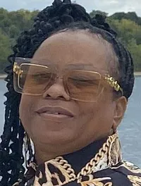 Six women are posing together on a deck with a cloudy sky and water in the background.