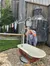 A person is splashing water on their face using a makeshift outdoor setup with a bucket, beside a rusted bathtub and laundry hanging nearby.
