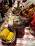 A table is set with a variety of Southern-style comfort foods, including fried chicken, corn on the cob, mashed potatoes, and a glass of iced drink, on a red-and-white checkered tablecloth.