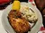 A plate features fried chicken, pulled pork, mashed potatoes, coleslaw, and a corn on the cob.