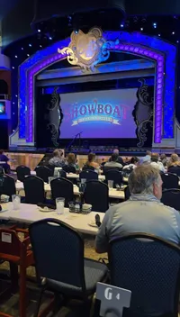 People are seated at tables facing a colorful stage with a sign that reads 