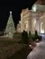 A beautifully lit Christmas tree stands beside an elegant building at night.