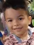 A young boy is smiling while standing beside a fish tank in a lush, indoor setting.