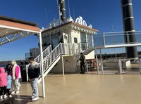 People are standing on the deck of a steamboat with intricate railings and a clear blue sky in the background.