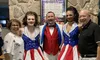 A group of five people, including three in sparkling red, white, and blue costumes, are posing together in front of a stone wall featuring a poster for 2024 celebrity concerts.