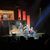 A band is performing on stage with a backdrop featuring rock posters and a large image of The Eagles' album cover.