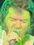 A performer dressed in a rhinestone-studded white jumpsuit sings into a microphone on stage under green lighting.