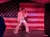 A performer dressed in an Elvis-inspired outfit sings in front of a large American flag backdrop.